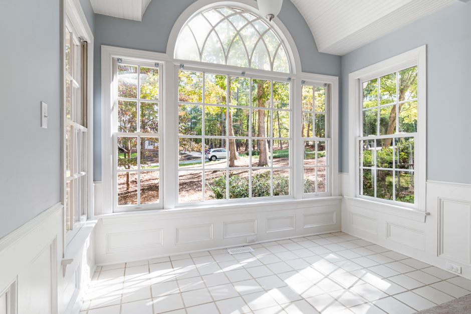 Bright empty room with tall paned windows, an arched top window and white wainscoting