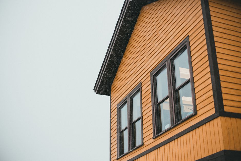 Two dark framed windows on a yellow wood sided house under an overcast sky