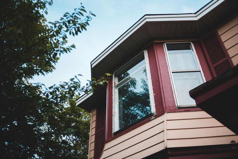 Corner bay window with a white frame on a house with red trim and cream siding, seen from below