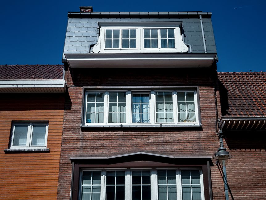 Brick house front with rows of white framed windows and a dormer under a blue sky