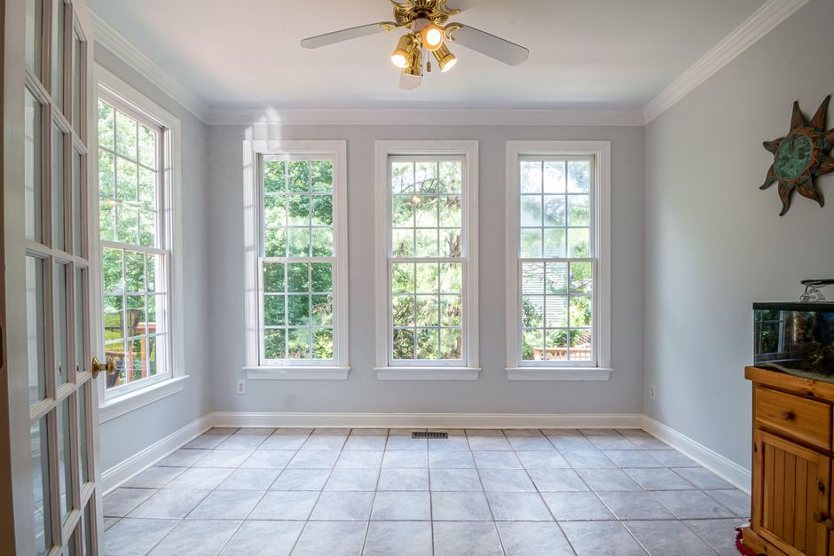 Empty room with three tall double hung windows, a ceiling fan and a tile floor