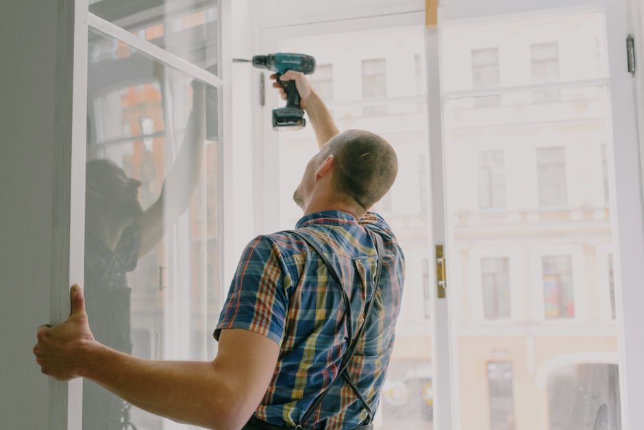 Worker in a plaid shirt using a cordless drill on a white window frame