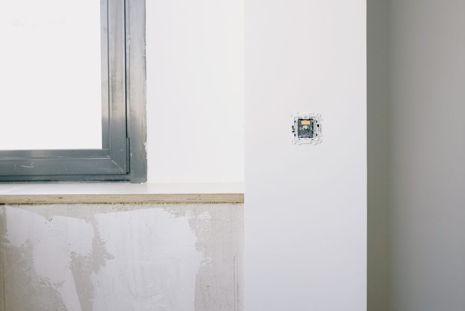 Interior corner with a dark metal window frame, a bare sill and an electrical switch on a white wall